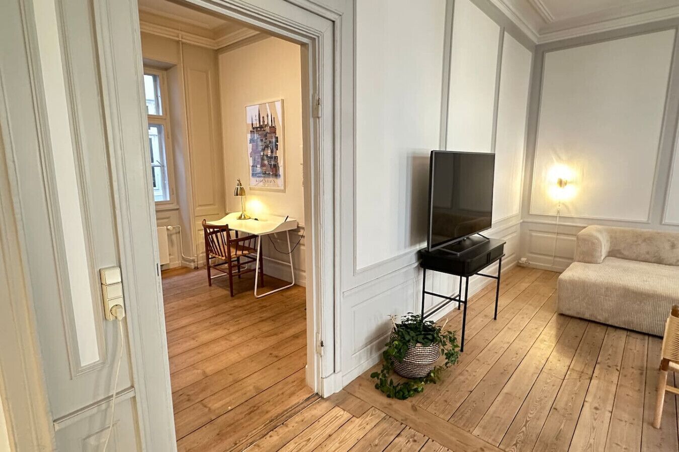 A living room with a TV, a sofa, a dining area with a table and chairs, and a potted plant.