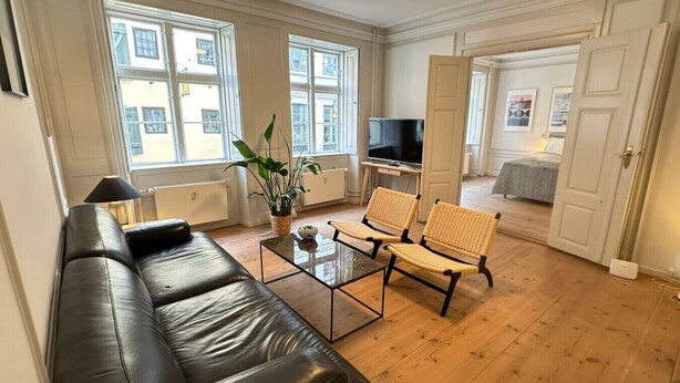 A modern living room with a black leather sofa, wicker chairs, a glass coffee table, and a TV.