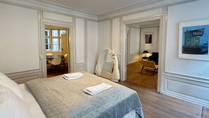 A hotel room with a bed, a chair, a desk, and a door leading to a dining area.