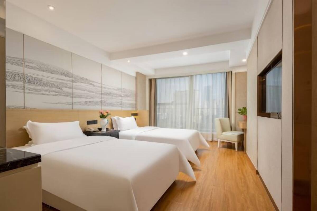 A hotel room with two beds, a desk, a chair, a TV, and a large abstract painting on the wall.