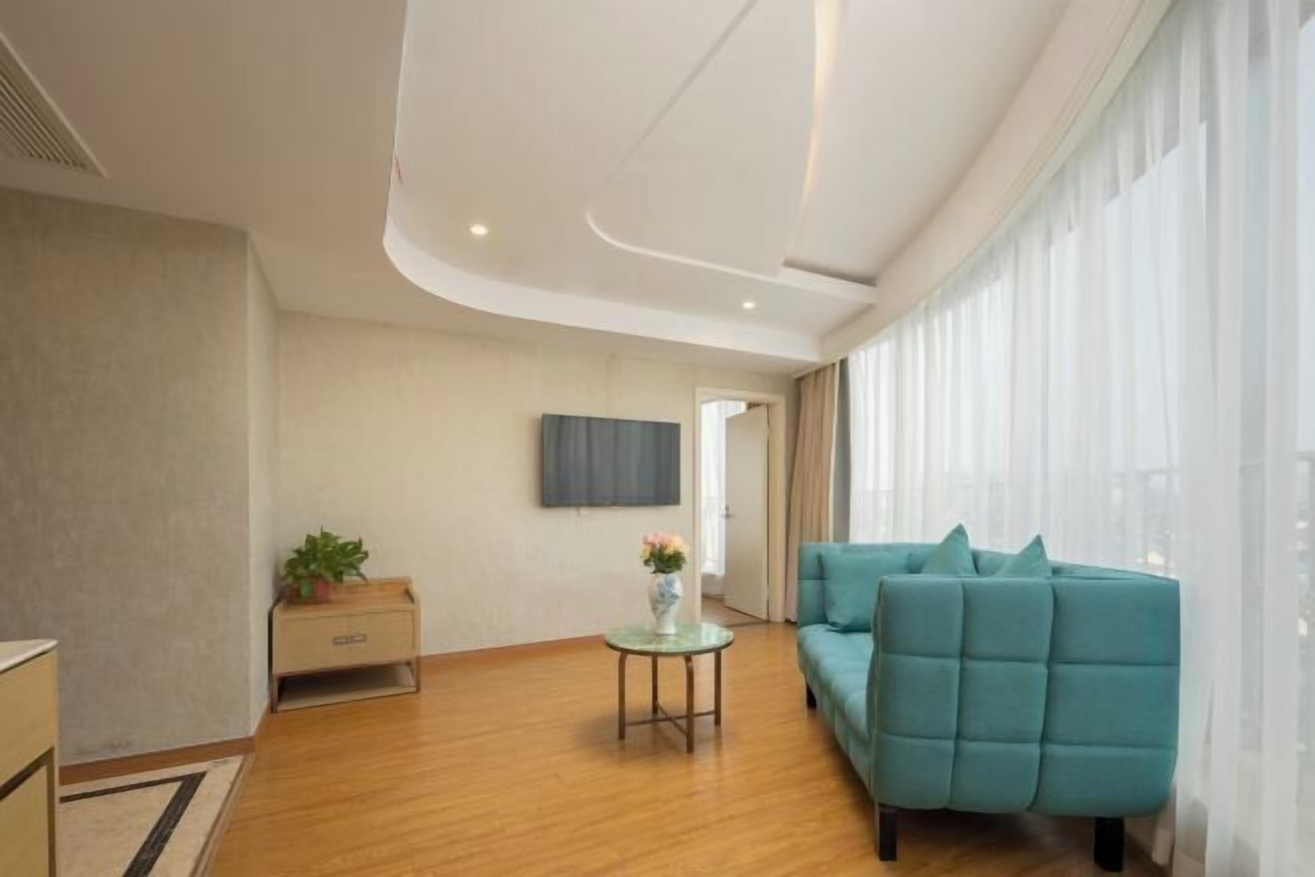 Un salon moderne avec un canapé de couleur turquoise, une petite table ronde ornée d’un vase et un téléviseur à écran plat fixé au mur.