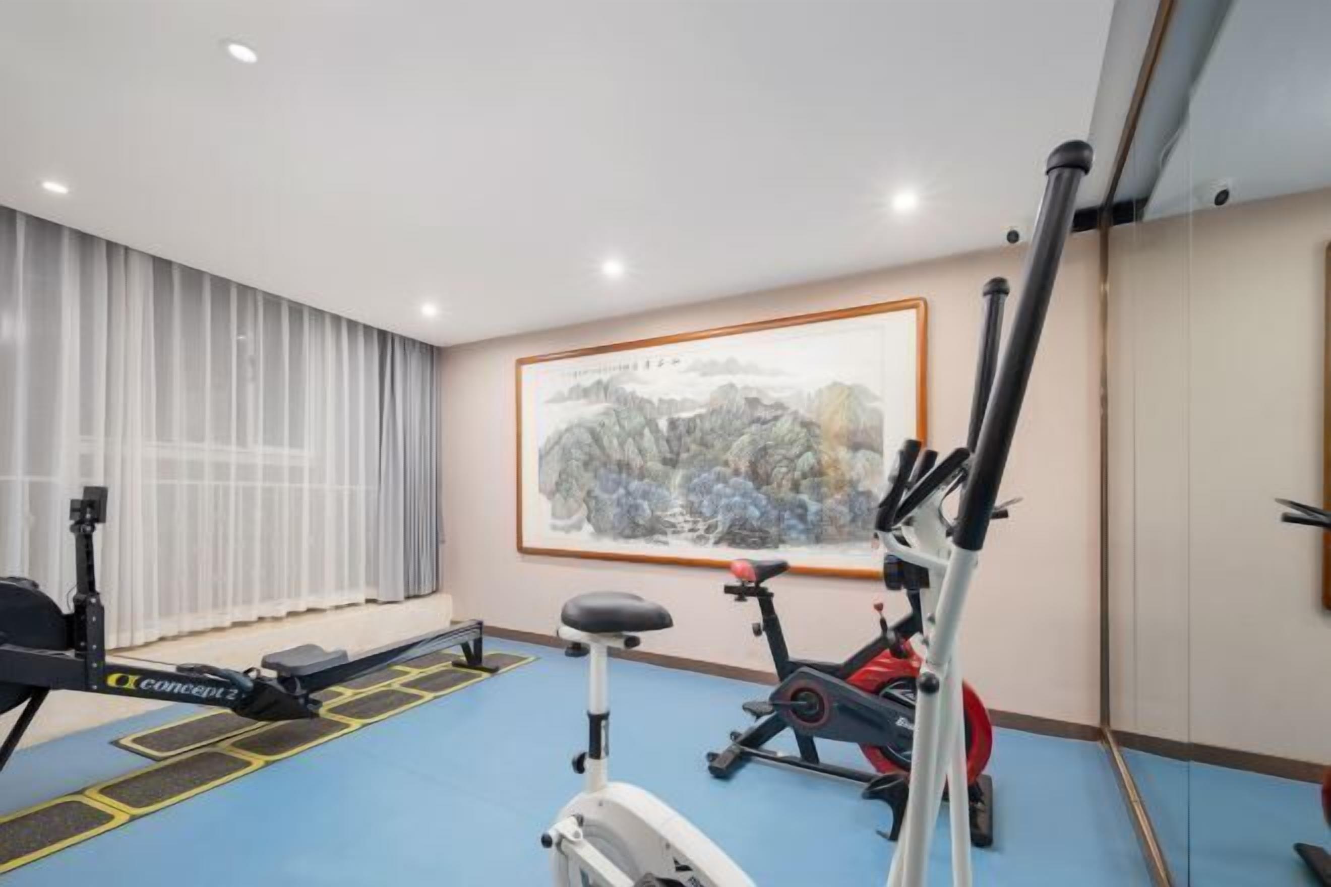 A gym with exercise equipment, a blue floor, and a large painting on the wall.