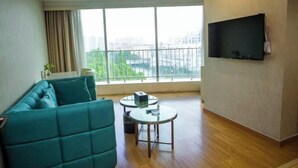 A modern living room with a teal sofa, a small round table, and a TV mounted on the wall. - Metropolo Jinjiang Hotel(Kunshan Jinying international Kunju theater store) (Kunshan)