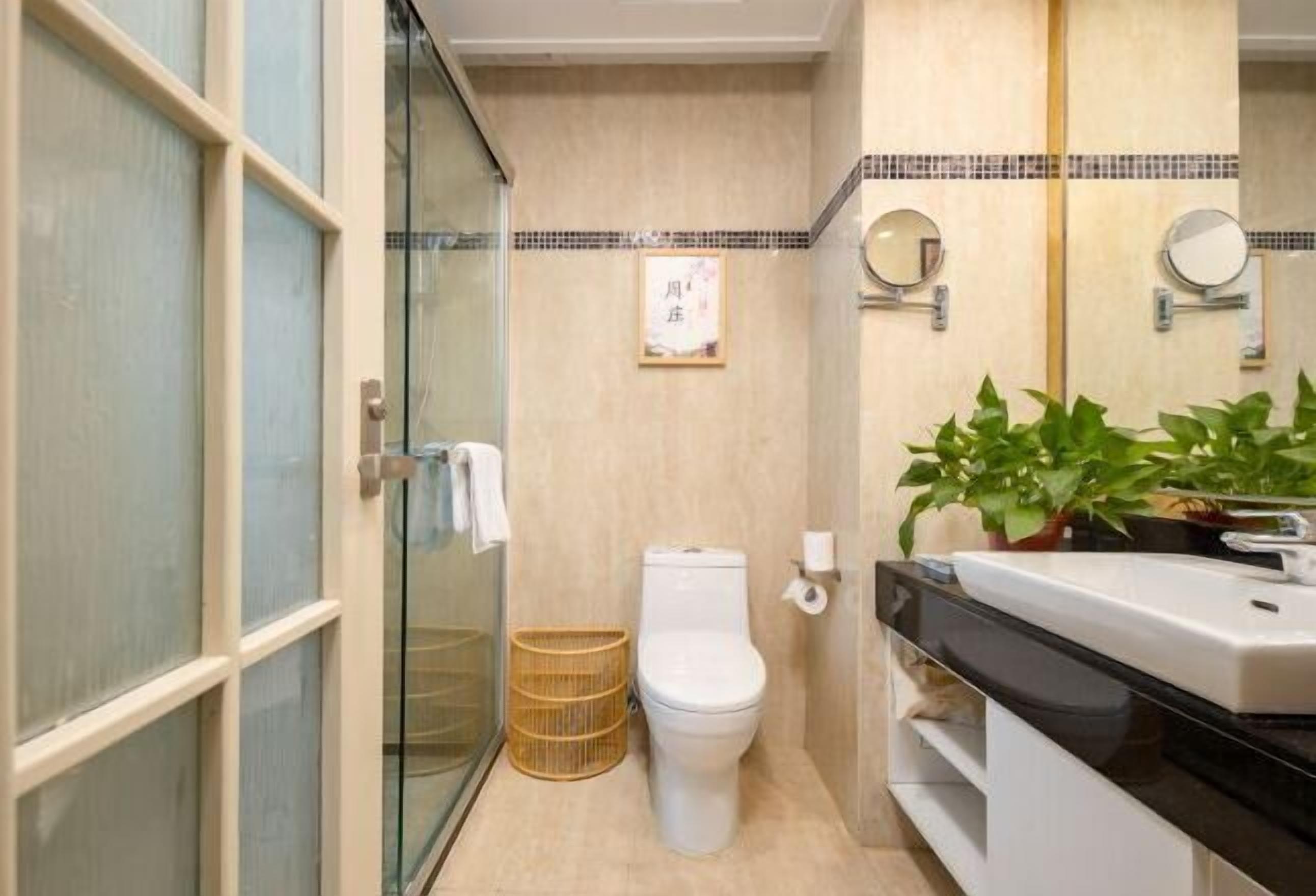 Une salle de bain comprenant des toilettes, un lavabo, un miroir, un tableau encadré accroché au mur et une plante en pot.