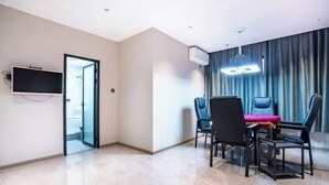 Une chambre d’hôtel moderne dotée d’un téléviseur à écran plat fixé au mur, d’une porte vitrée donnant sur un escalier, d’un coin repas avec une table et des chaises, et d’une grande fenêtre avec des rideaux.