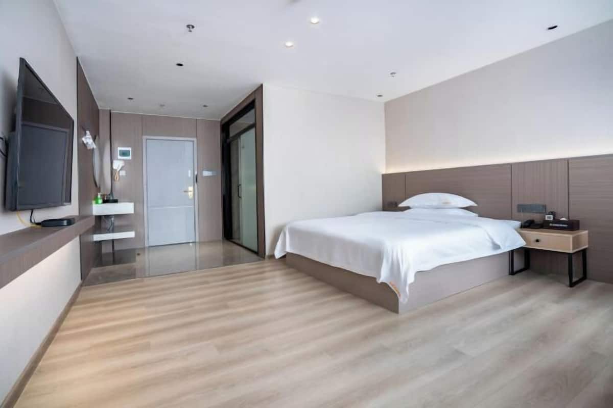Una camera d'albergo moderna con un letto grande, un comodino, una televisione a schermo piatto montata a parete e una porta scorrevole che dà su un bagno.