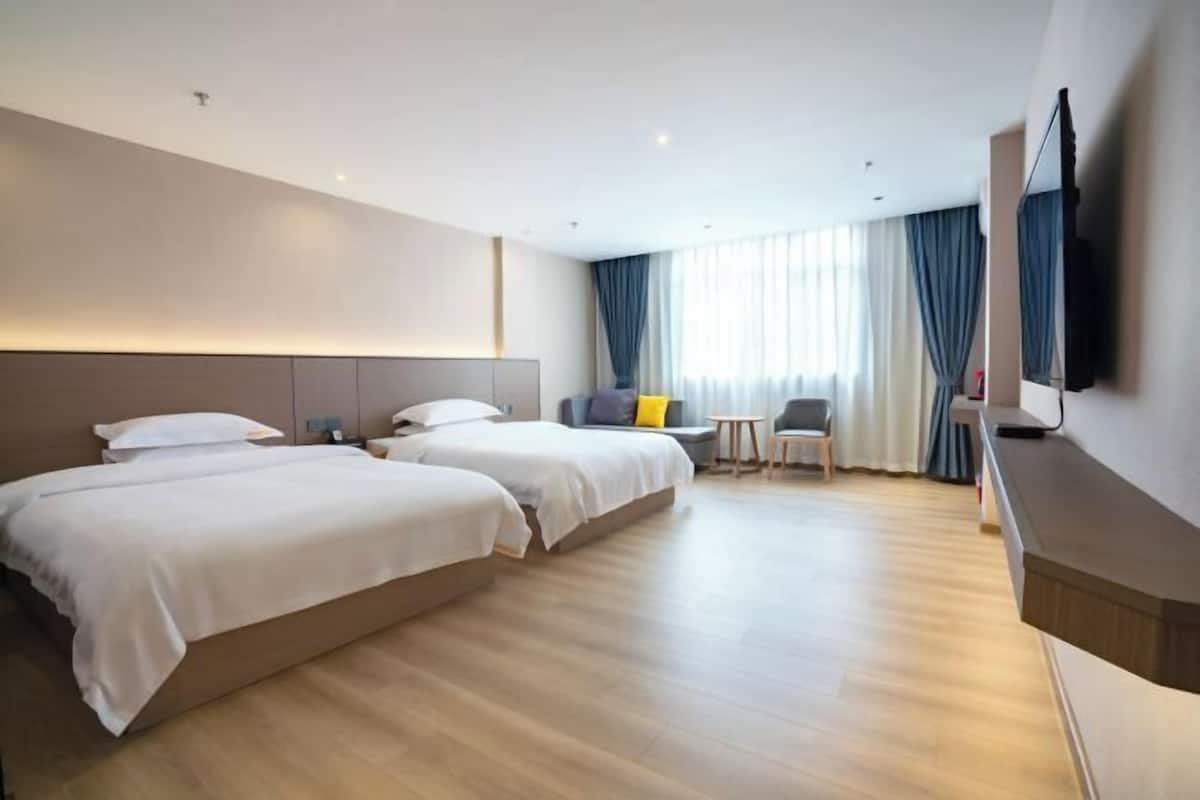 Camera d'albergo moderna con due letti, un piccolo angolo salotto e una TV a parete.