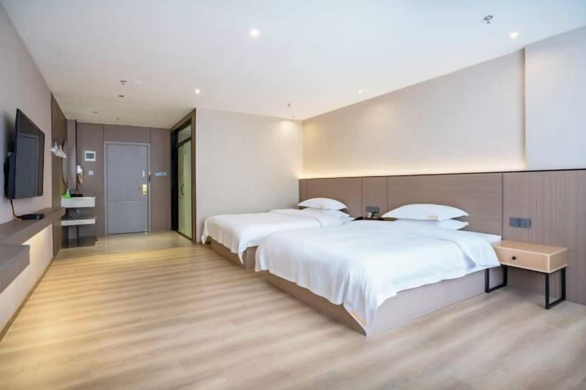 Una camera d'albergo moderna con due letti, una TV a schermo piatto, un comodino e un pavimento in legno.