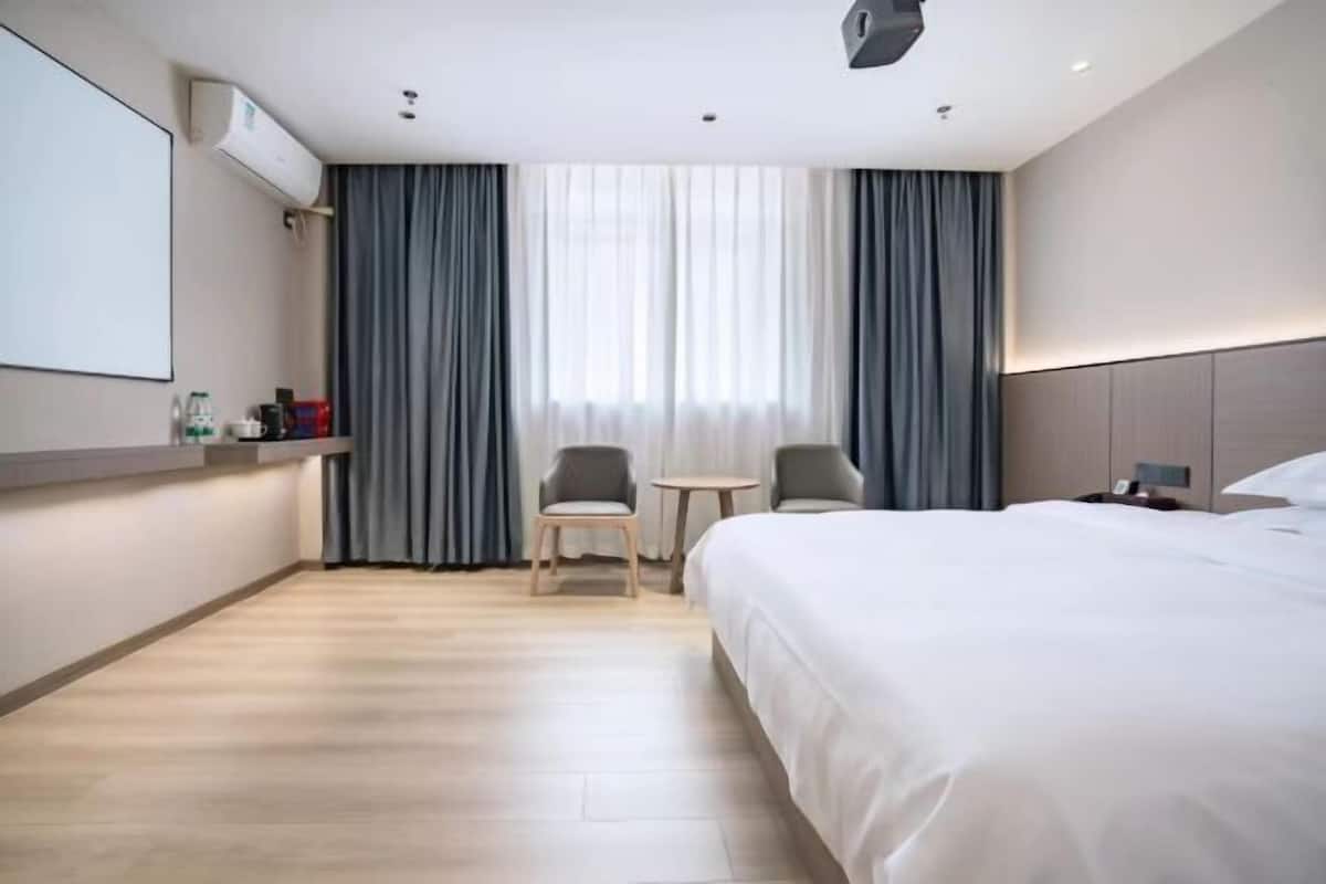 Una camera d'albergo con un letto, due sedie, un tavolino, una televisione e una finestra con tende.