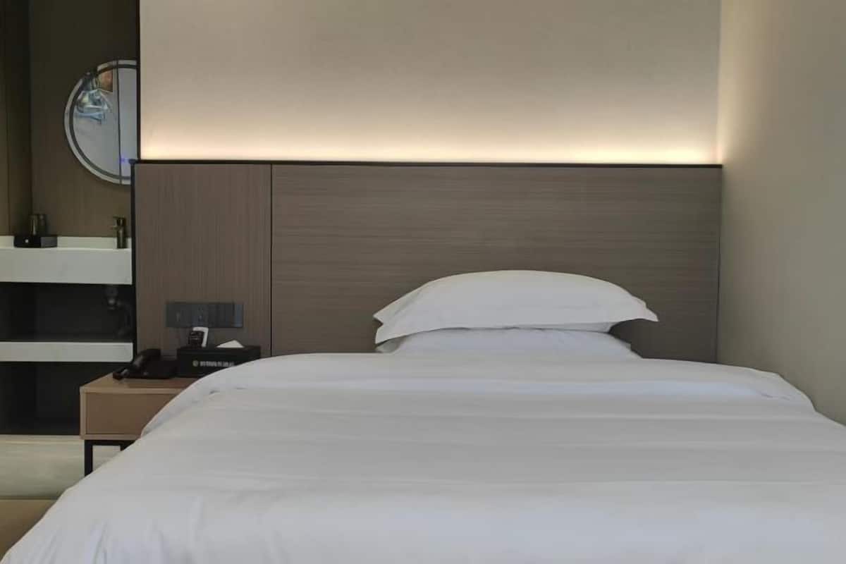 Una camera d'albergo moderna con un letto rifatto, un comodino con una lampada e uno specchio fissato alla parete.