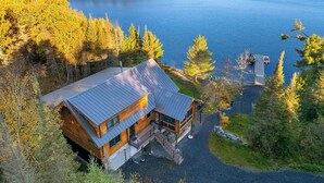 Mökki, jonka katto on tehty metallista, ja jonka ympärillä on puita ja järvi.