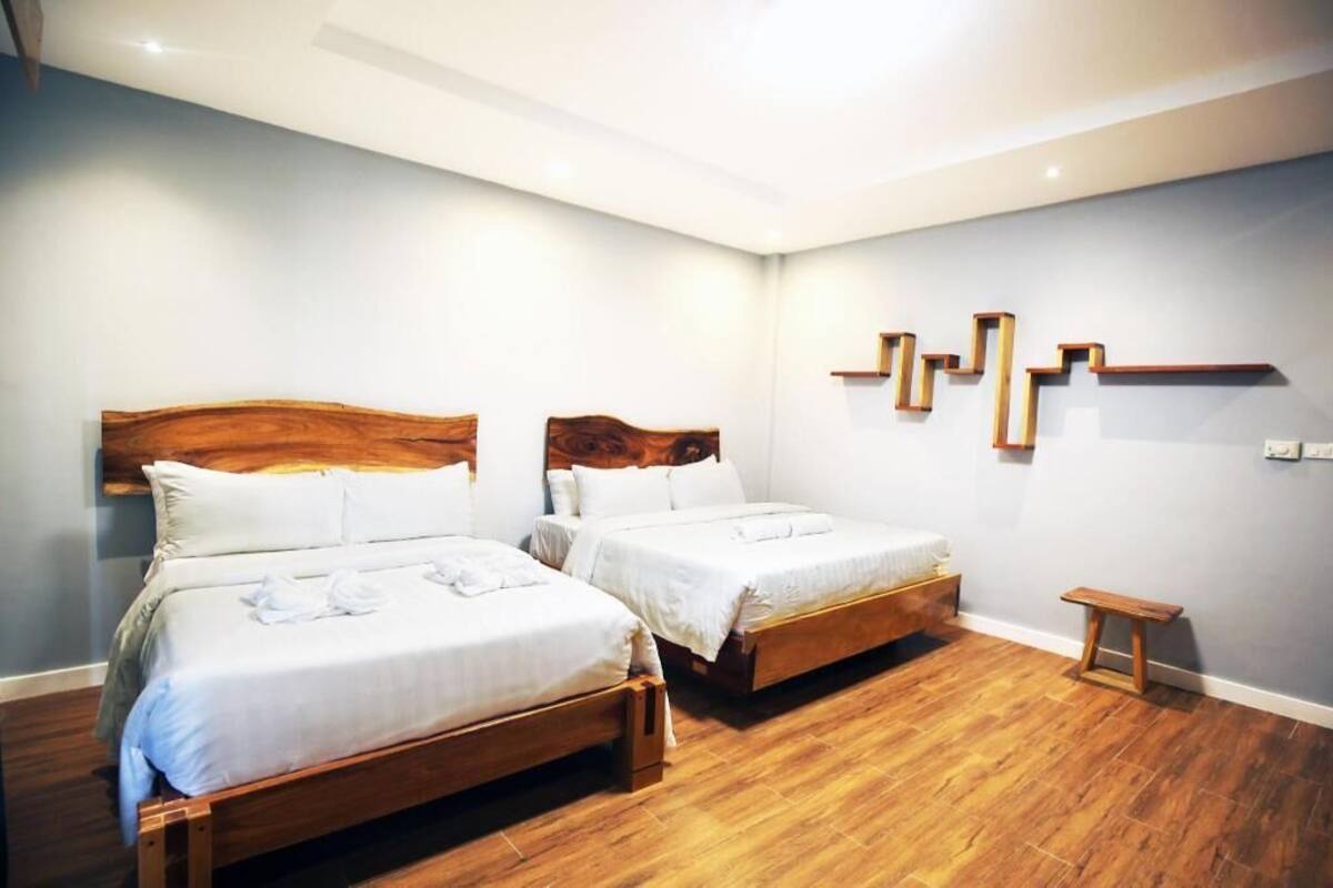 A hotel room with two wooden beds, a small wooden bench, and a wall-mounted shelf.