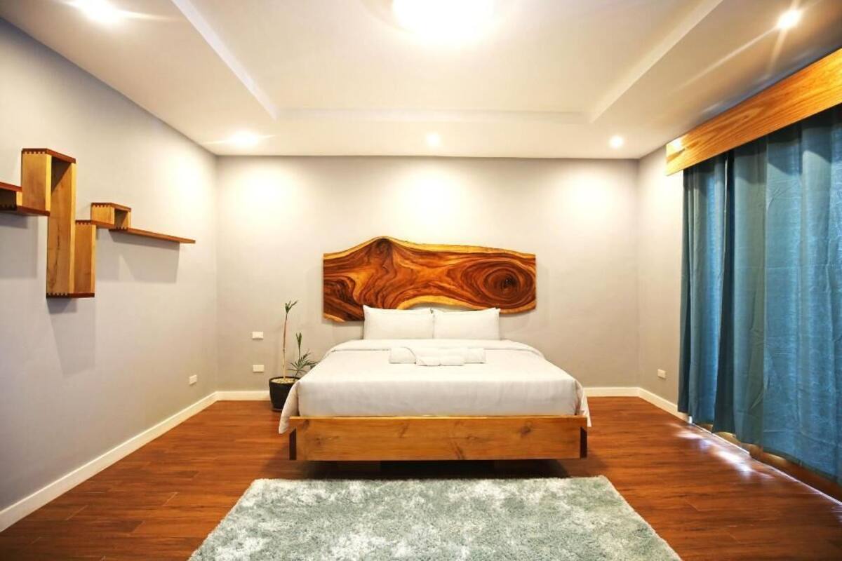 A bedroom with a wooden headboard, a bed with white bedding, a green rug, and a potted plant.