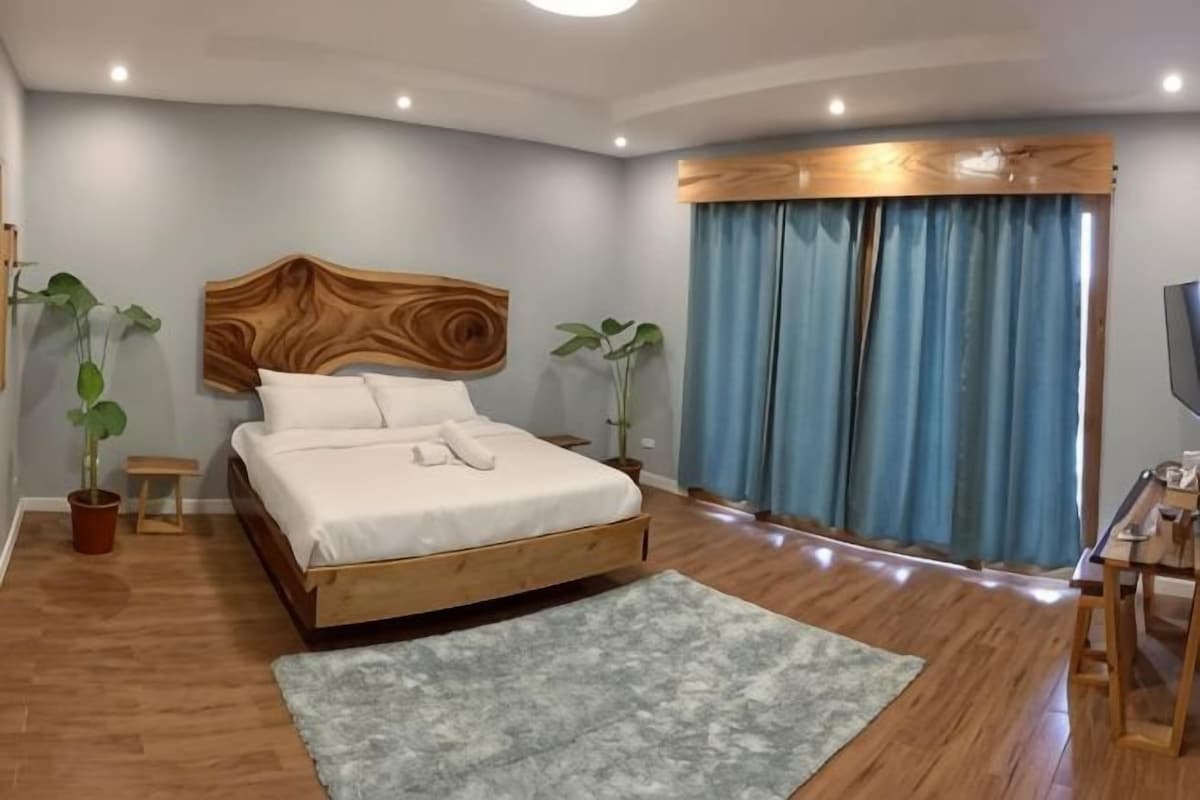A modern bedroom with a wooden bed, a large window with curtains, and a flat-screen TV.