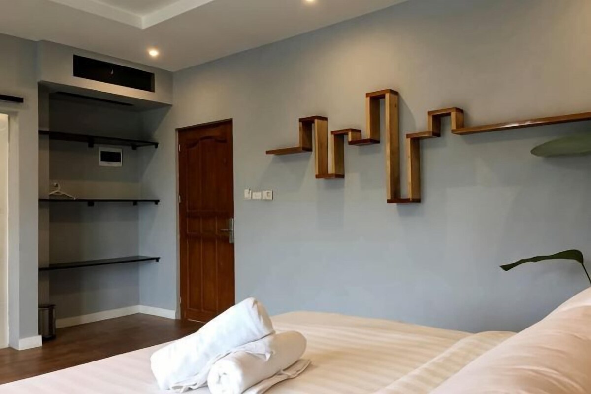 Un dormitorio con cama, una puerta de madera, un estante en la pared y una planta.