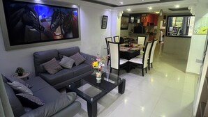 A modern living room with a grey sofa, a glass coffee table, and a dining area with a table and chairs. - Casa Villa Carolina 5 min Puerta de Oro (Barranquilla)