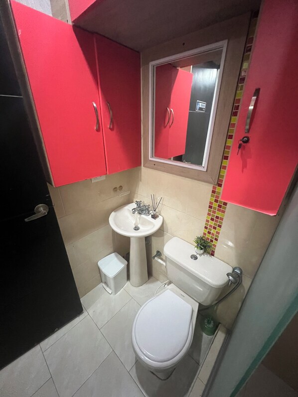 A compact bathroom with a white toilet, a pedestal sink, and red cabinets. - Casa Villa Carolina 5 min Puerta de Oro (Barranquilla)