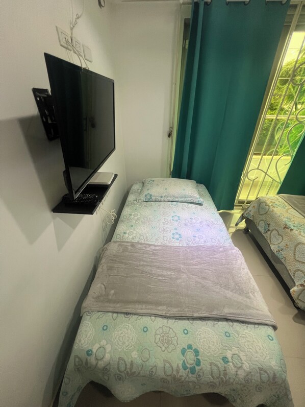 A small room with a bed, a TV on a stand, and a window with curtains.