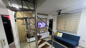 A modern living room with a blue sofa, a TV, a staircase, and a ceiling fan. - Casa Villa Carolina 5 min Puerta de Oro (Barranquilla)