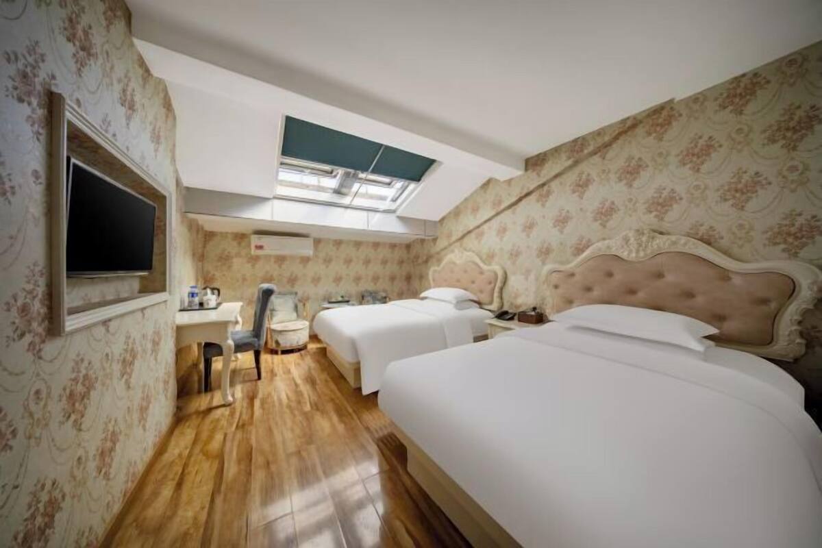 Un dormitorio con dos camas, un escritorio, una silla, un televisor y un tragaluz.