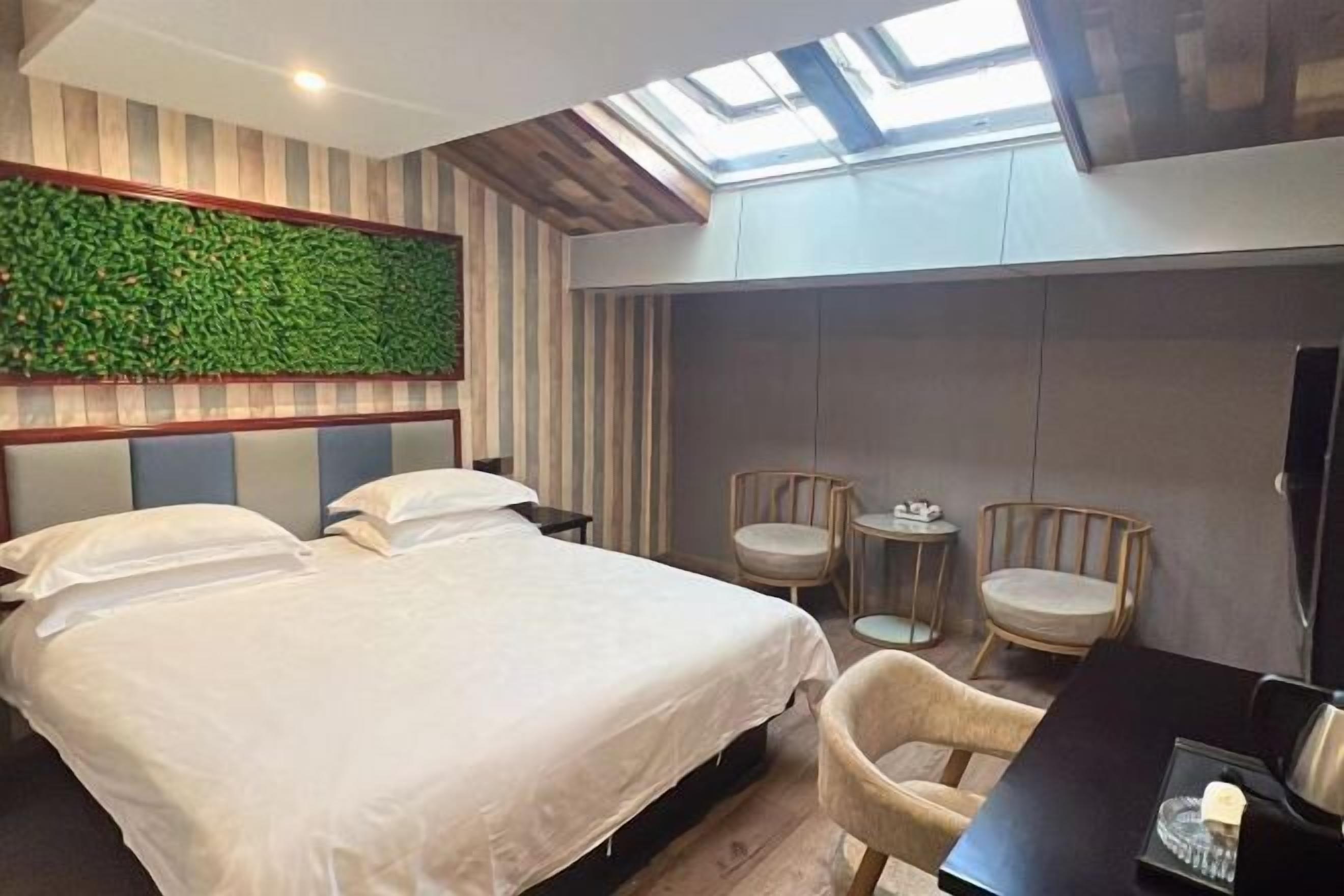 Une chambre d’hôtel avec un lit, deux chaises, une petite table, un téléviseur et un mur vert.