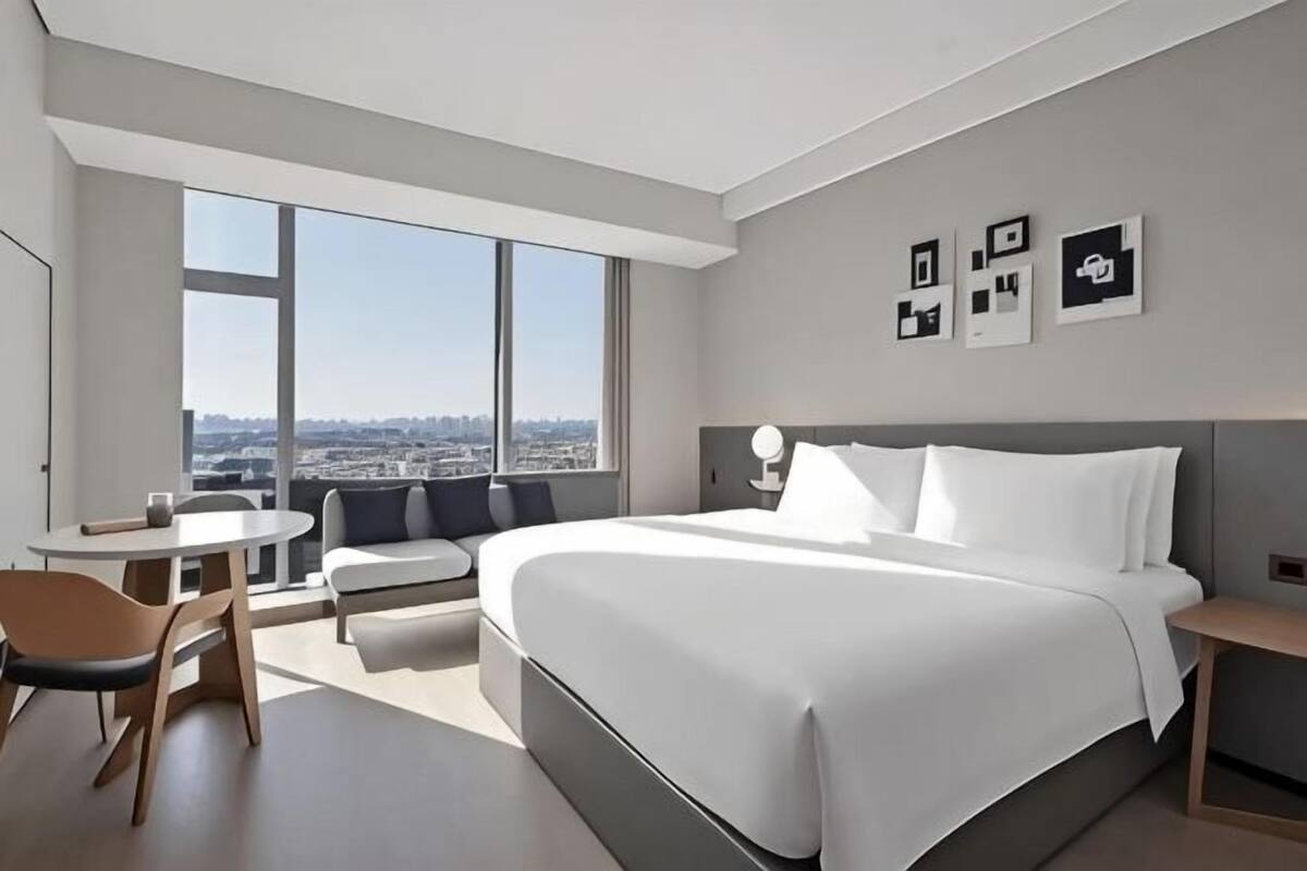 Una habitación de hotel moderna con una cama grande, un área de descanso, una mesita y vistas a la ciudad.