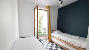 A room with a checkered floor, a bed with white bedding, a white table, and a window with a curtain.