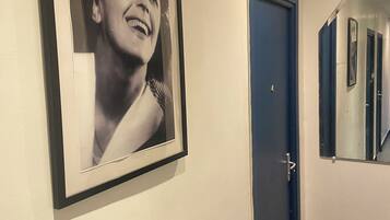 Un pasillo con una fotografía enmarcada en la pared, una puerta azul cerrada y un espejo que refleja parte del pasillo.