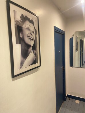 Ein Flur mit einem gerahmten Foto an der Wand, einer geschlossenen blauen Tür und einem Spiegel, der einen Teil des Flurs reflektiert.