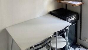 A corner of a room with a white desk, a black heater, and shelves with flowers and a white kettle.