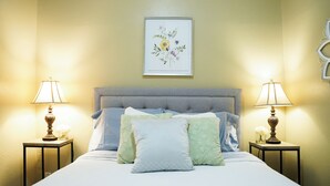 A neatly made bed with a grey headboard, flanked by two bedside tables with lamps, and a framed floral artwork above. - Historic 3-bedroom house close to downtown Guthrie.  (Guthrie)