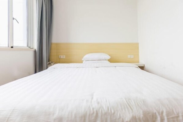 A hotel room with a bed, a nightstand, a lamp, a window with curtains, and a wall with a light switch. - Haitian Hotel (Zhoushan Shenjia Branch) (Zhoushan)