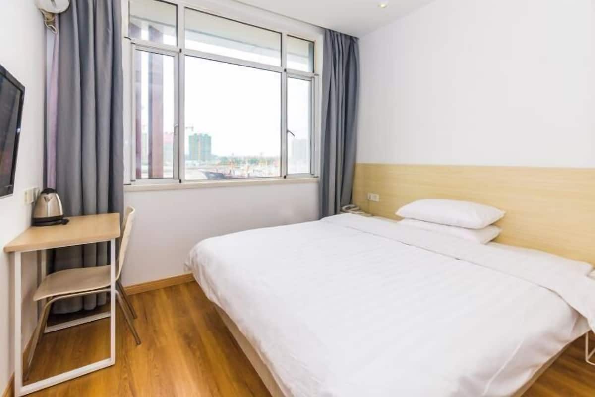 Quarto de hotel com cama, escrivaninha e janela com cortinas.