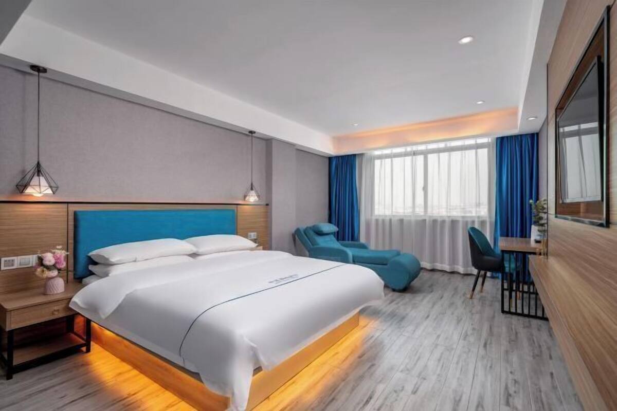 Ein modernes Hotelzimmer mit einem großen Bett, einem Schreibtisch, einem Massagesessel und Blick auf die Stadt.