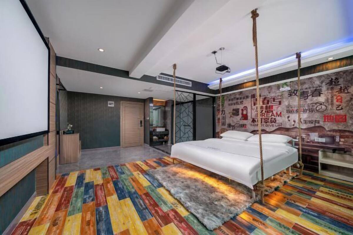 Ein modernes Hotelzimmer mit einem Bett, einem farbenfrohen Streifen Teppich, einem großen Spiegel und einer Wand mit Motivationspostern.