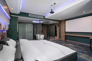 A modern hotel room with a large bed, a projector screen, and a seating area with a sofa and chairs. - Guangzhou Baisi Elegant Hotel (Huadu Shiling) (Guangzhou)