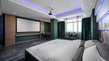 A hotel room with a large bed, a flat-screen TV, a desk, and a seating area with curtains.