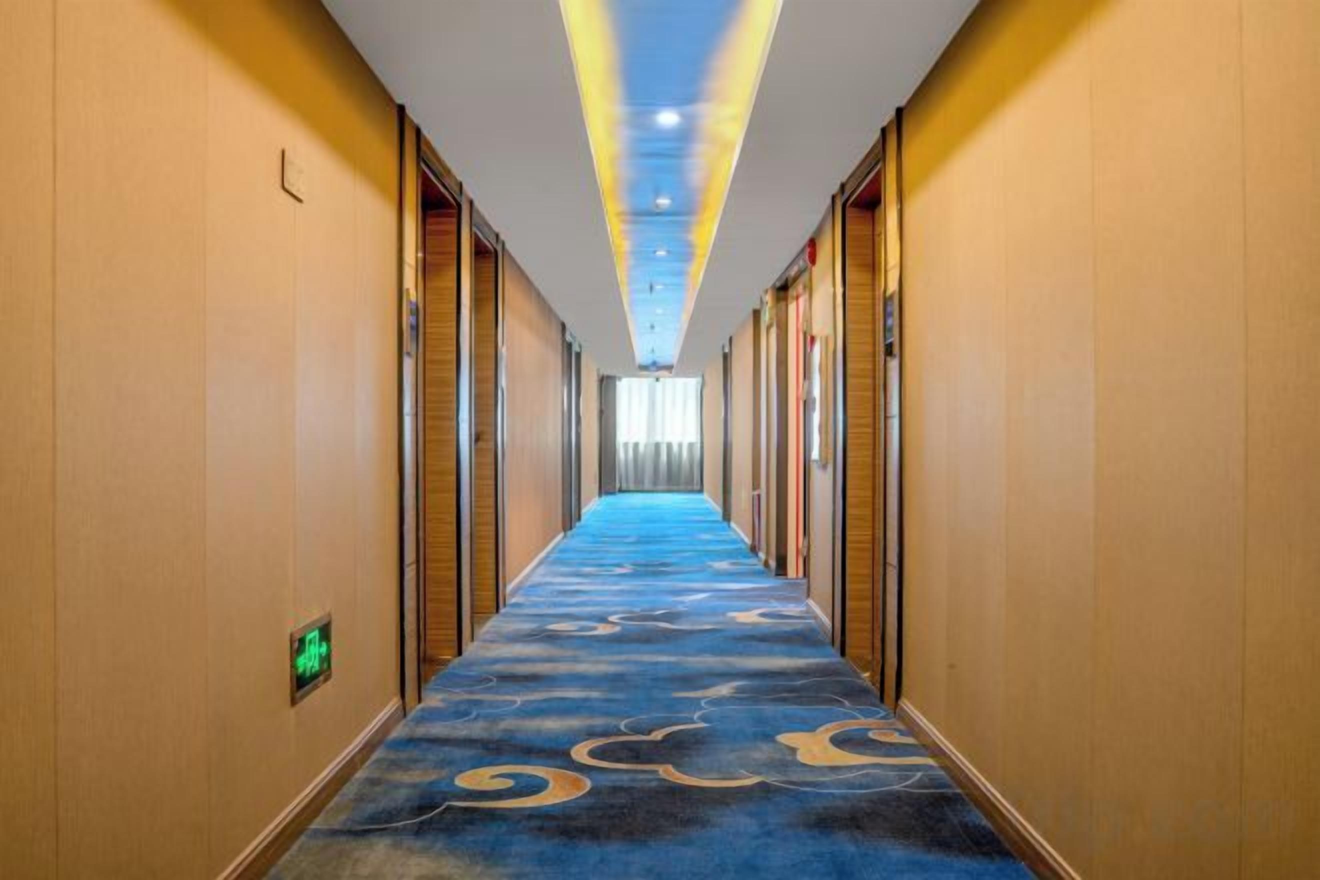 A hotel corridor with a blue carpet, wooden doors, and a ceiling with recessed lighting.
