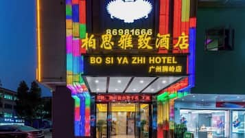 A hotel entrance with a neon sign, a crown logo, and a sign indicating it's a hotel.