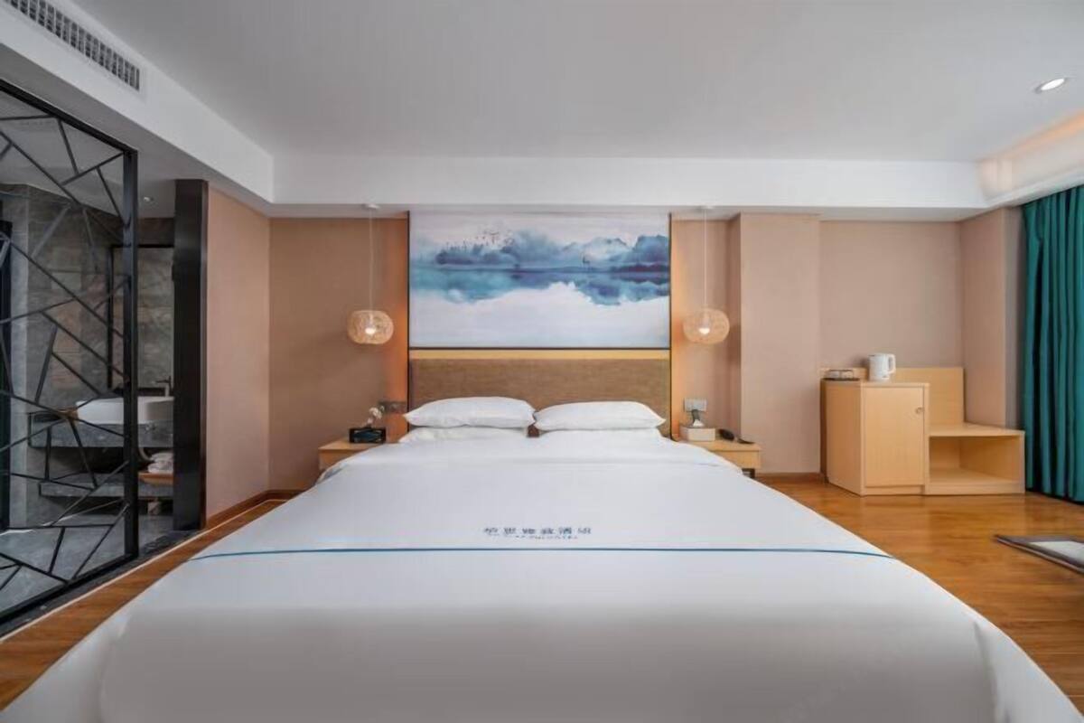 Ein modernes Hotelzimmer mit einem großen Bett, einem Gemälde an der Wand und einem hölzernen Nachttisch.