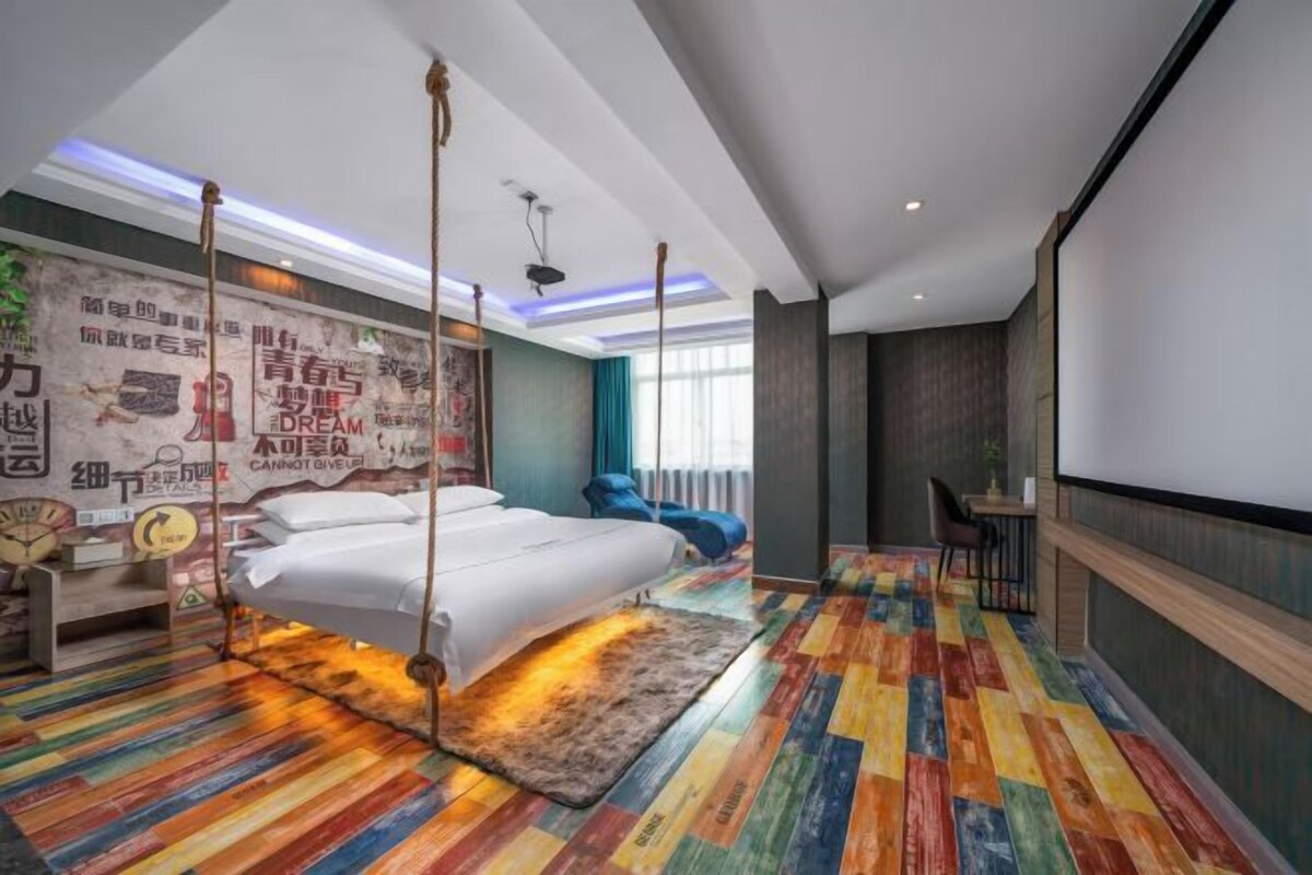 A modern bedroom with a bed, a desk, and a chair. There is a colorful striped floor and a large window.