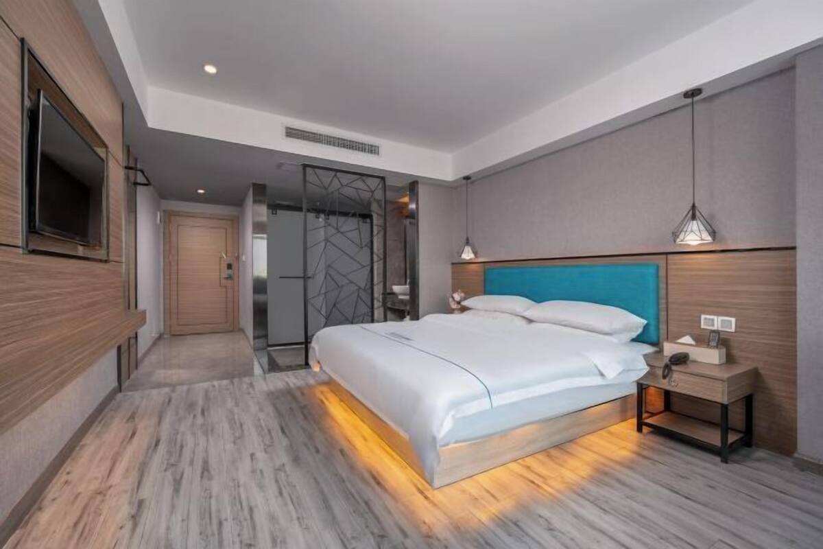 Ein modernes Hotelzimmer mit einem großen Bett, einem an der Wand montierten Fernseher und einem begehbaren Kleiderschrank.