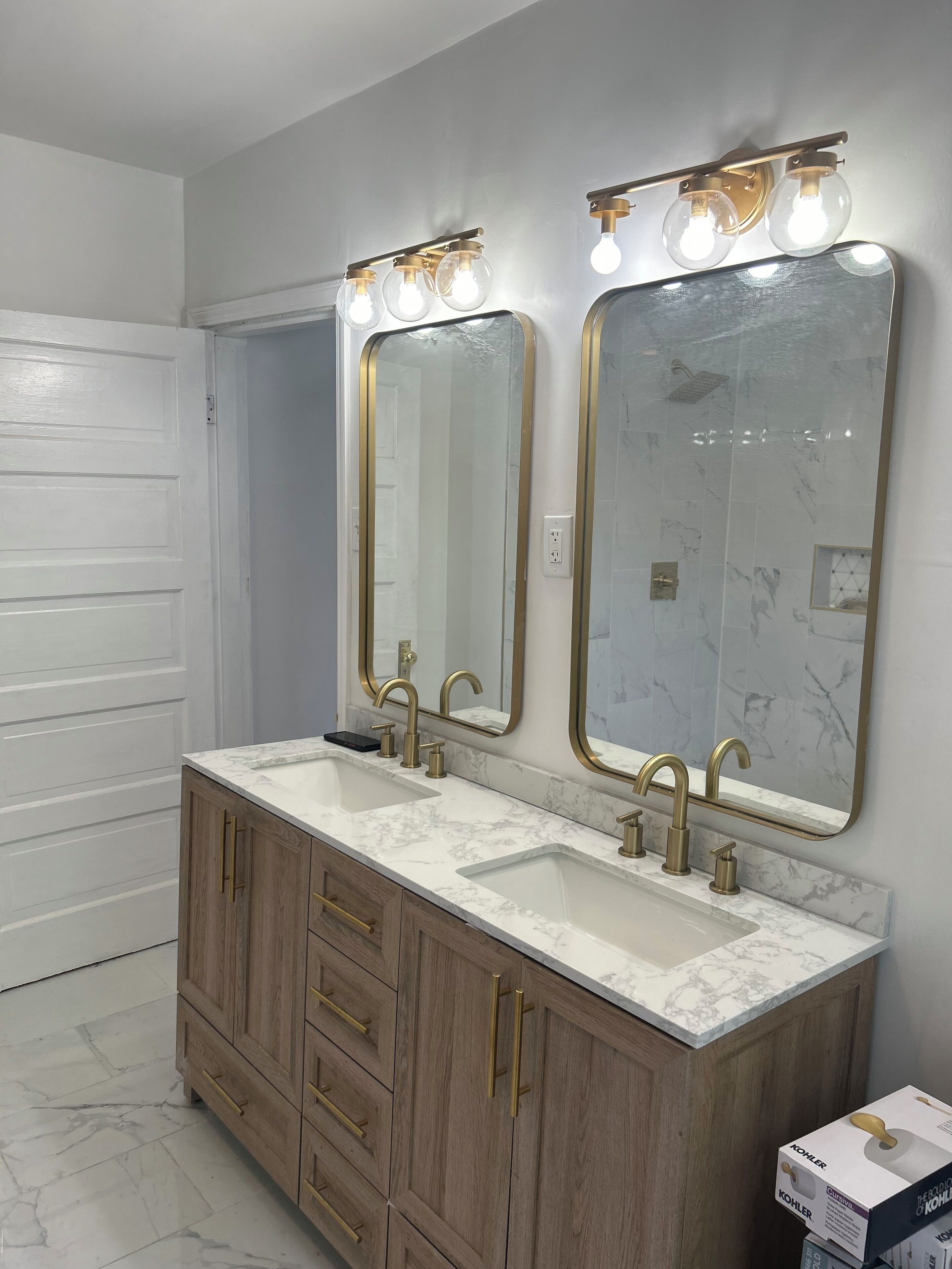 A bathroom with two sinks, wooden cabinets, marble countertops, and a large mirror with a gold frame.