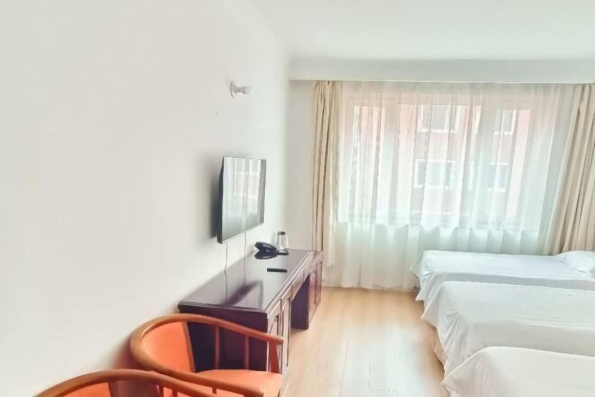 A hotel room with a bed, a desk, a chair, a TV, and a window with curtains.