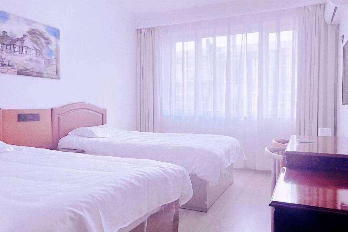 A hotel room with two beds, a painting on the wall, and a large window with curtains.