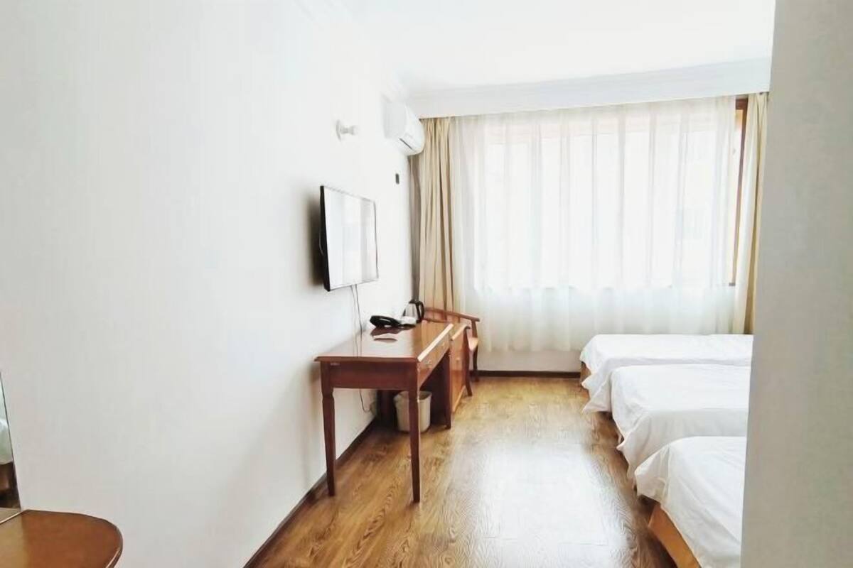A hotel room with a wooden desk, a flat-screen TV, and two single beds.