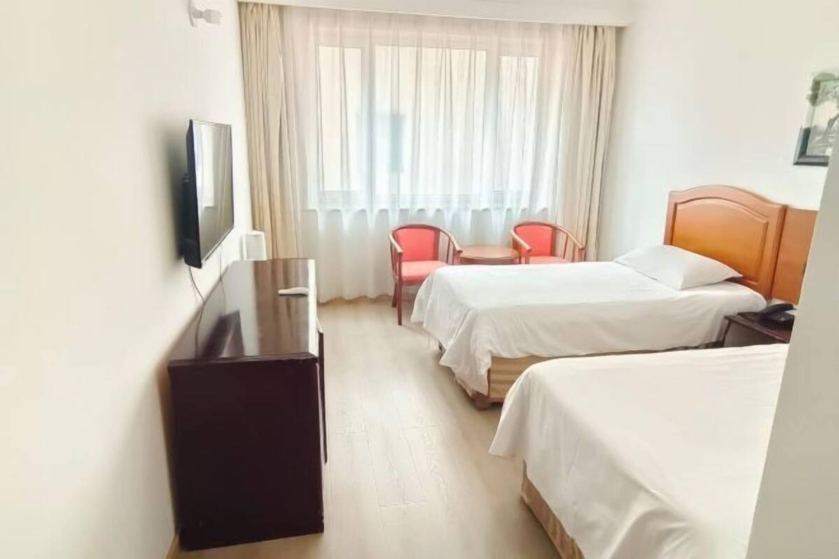 A hotel room with two beds, a desk, a chair, and a TV.