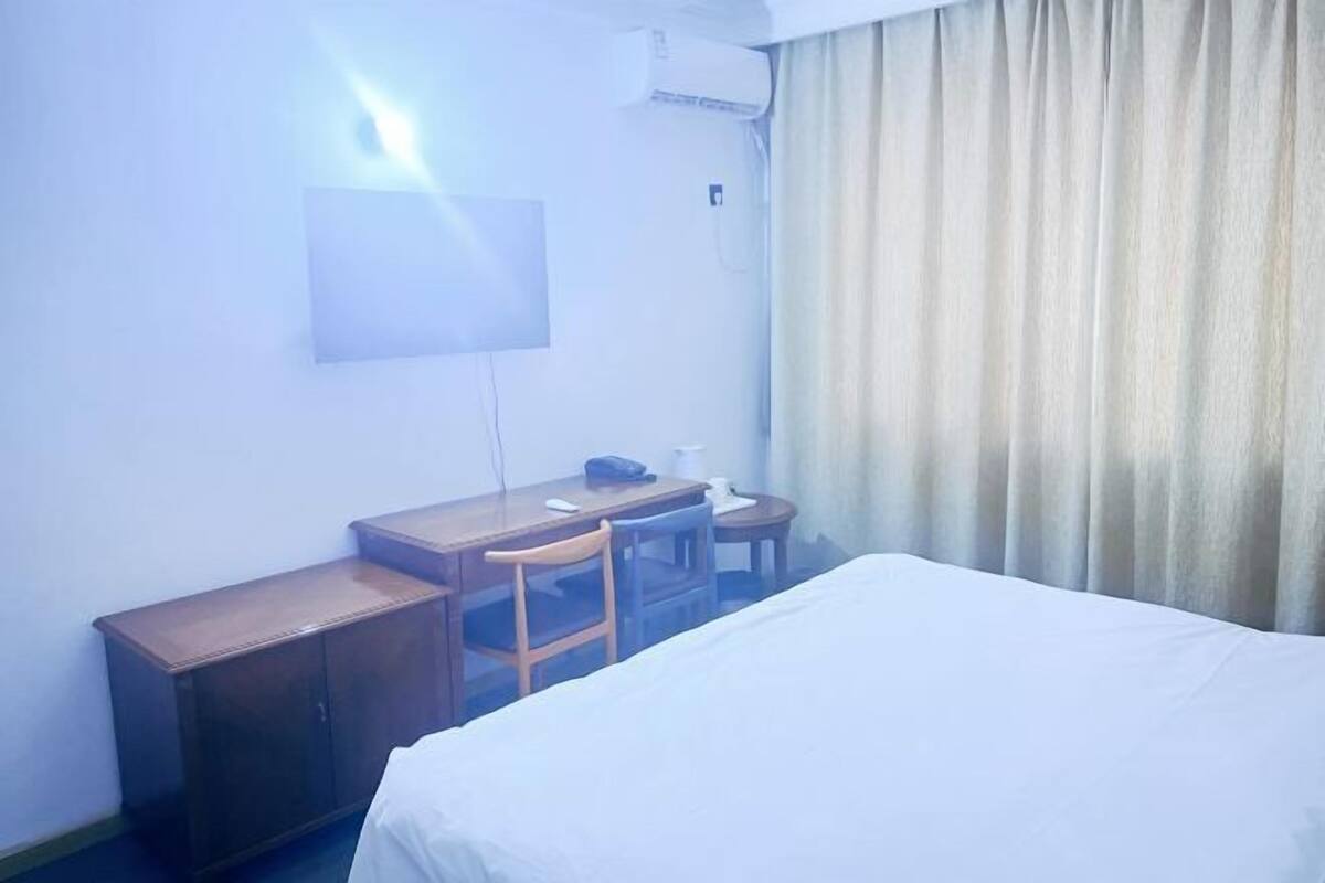 A hotel room with a bed, a desk, a chair, a lamp, and a curtain.