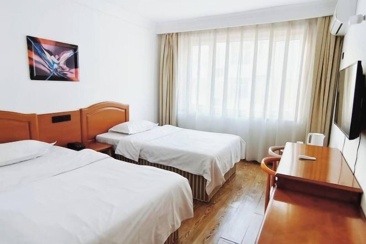 A hotel room with two beds, a wooden desk, a television, and a window with curtains.