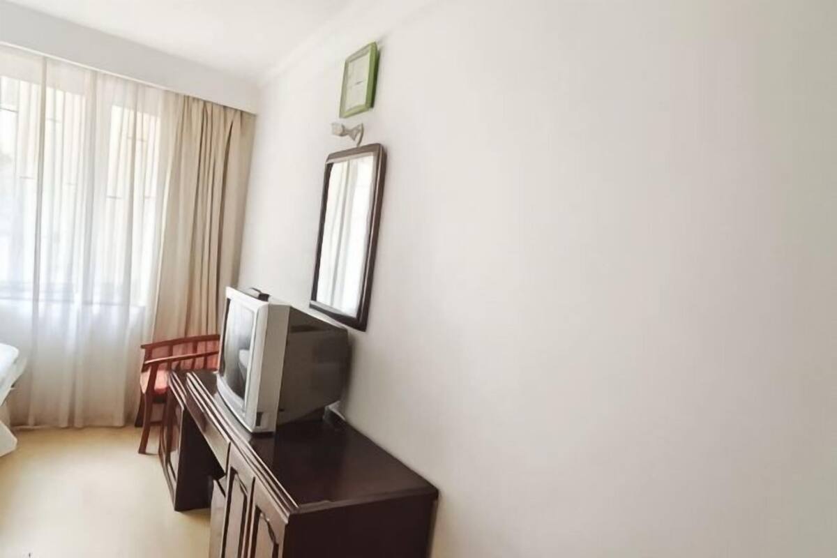 A hotel room with a bed, a desk with a television, a chair, and a window with curtains.